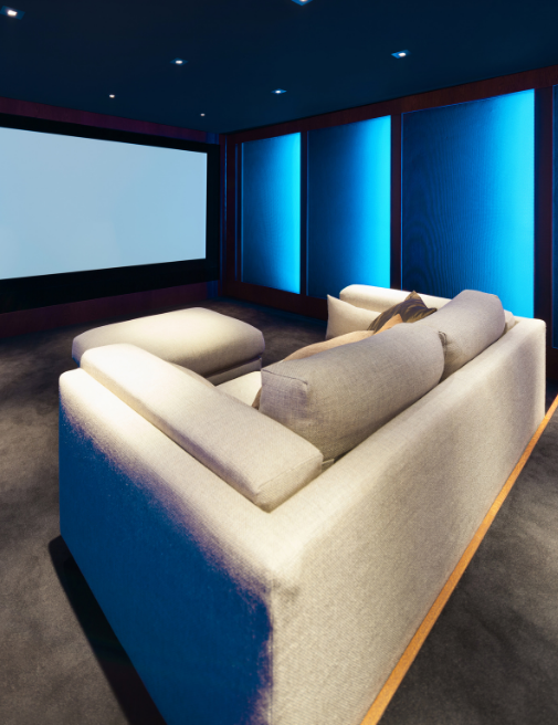 Vertical view of a custom home cinema featuring tiered seating, a large projection screen, surround sound speakers, and ambient lighting.
